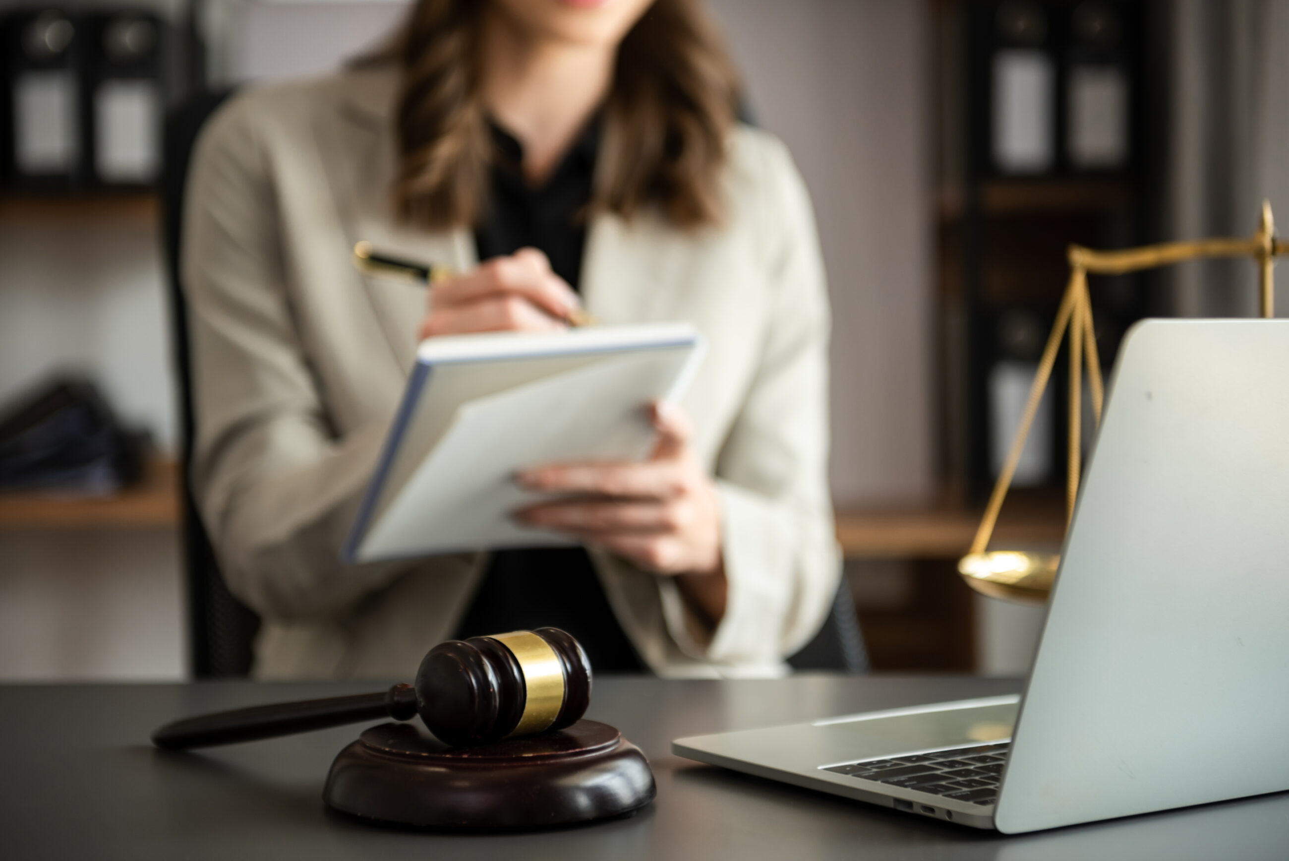 Kobieta analizująca dokumenty prawne przy biurku, obok młotek sędziowski i laptop — symbol pracy nad zgodnością prawną stron i sklepów internetowych.